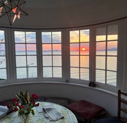 A dining room with a table and flowers overlooking the ocean at Murmur Y Don in Harlech