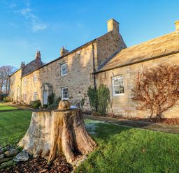 Stone cottages with chimneys and a tree stump in the grassy yard at East Farm House in Humshaugh near Hexham