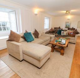 A sitting room with beige sofas, wooden coffee table, cushions, and windows at East Farm House in Humshaugh near Hexham