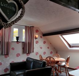 A sitting area with a black sofa a round wooden table with chairs floral wallpaper and a skylight window at The Coach House in North Newton near Bridgwater
