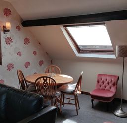 A dining area with a round wooden table and four chairs next to a slanted window and a pink armchair with a floor lamp at The Coach House in North Newton near Bridgwater