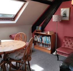 A room with a wooden dining table and chairs and a bookshelf against a red wall at The Coach House in North Newton near Bridgwater