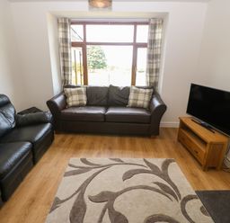 A living room with two sofas a TV on a wooden stand and a patterned rug at Y Berth Ddu Farmhouse in Clynnog Fawr