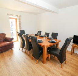 A dining room with a wooden table set for eight with black chairs a leather armchair and a television on a unit at Y Berth Ddu Farmhouse in Clynnog Fawr