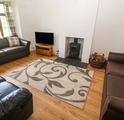 A living room with leather sofas a patterned rug a wood stove and a television at Y Berth Ddu Farmhouse in Clynnog Fawr