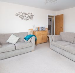 A living room with two sofas a wooden cabinet two chairs and an open door at The Moorings in Deganwy near Llandudno