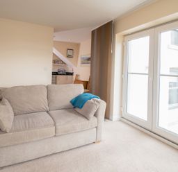 A living room with a beige sofa and blue throw next to glass doors at The Moorings in Deganwy near Llandudno