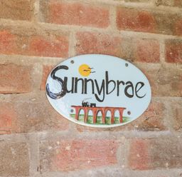 An oval ceramic sign with the word Sunnybrae and a drawing of a train on a bridge attached to a brick wall at Sunnybrae in Whitby