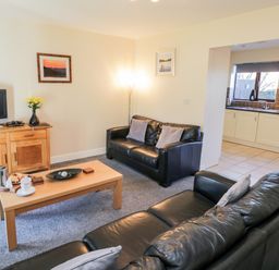 A living room with black leather sofas a wooden coffee table a wooden TV stand a television and an open doorway to a kitchen at Sunnybrae in Whitby