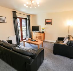 A living room with two black leather sofas a wooden coffee table a wooden cabinet a television and curtains at Sunnybrae Whitby