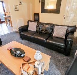 A living room with black leather sofas a wooden coffee table with pastries and a coffee pot at Sunnybrae Whitby