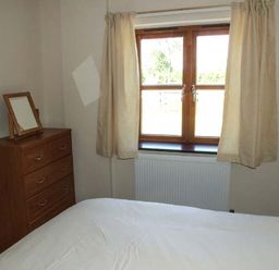A bedroom with a bed white bedding wooden chest of drawers with a mirror and a window with beige curtains at Dovetail in Westbury-on-Severn
