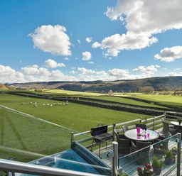 An outdoor deck with tables chairs and a barbecue overlooking a green field with sheep and hills at Browside in Little Arrow near Coniston