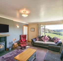 A living room with sofas a red armchair a wood stove and a large window showing fields at Browside Little Arrow near Coniston