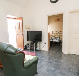 A living room with green leather chairs a wooden door a television and a view into a bedroom at Yr Hen Ysgubor in Trelech near St Clears