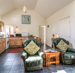 A kitchen with wooden cabinets and two green armchairs with cushions at Yr Hen Ysgubor Trelech near St Clears