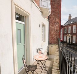 A small balcony with a round table and two chairs outside a green door overlooking a street with brick buildings at Nutshell in Whitby