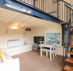 A small living area with a sofa table and chairs a television and spiral staircase at Nutshell in Whitby