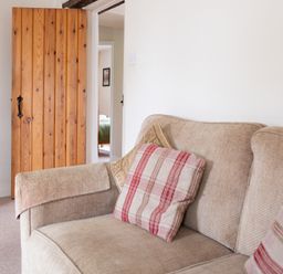 A beige sofa with patterned cushions beside a wooden door leading to a room with a bed at Crabtree in Hawkshead