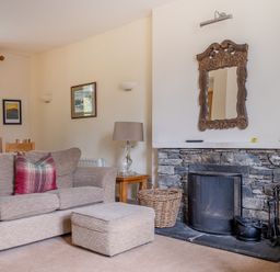 A living room with a sofa ottoman stone fireplace and a wooden framed mirror at Forge in Graythwaite near Hawkshead