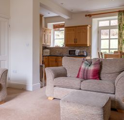 A living room with sofas and a kitchen area with wooden cabinets at Forge in Graythwaite near Hawkshead