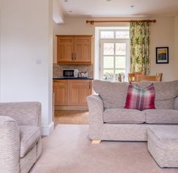A living room with sofas and plaid cushions next to a kitchen with wooden cabinets and a dining table at Forge in Graythwaite near Hawkshead