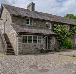 A stone building with external stairs and gravel in front with plants and a parked car at Newlands in Graythwaite near Hawkshead