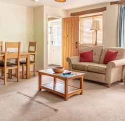 A living room with a wooden dining table and chairs a sofa with red cushions a coffee table and windows with blue curtains at Newlands Graythwaite near Hawkshead