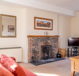 A living room with a stone fireplace a television on a stand and a red sofa at Greenhowes Graythwaite near Hawkshead