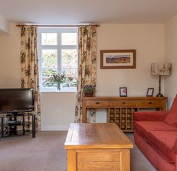 A living room with a red sofa wooden coffee table TV and floral curtains at Greenhowes in Graythwaite near Hawkshead