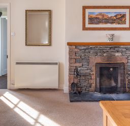 A living room corner with a stone fireplace a framed picture above a wooden mantel a mirror and a red sofa at Greenhowes Graythwaite near Hawkshead
