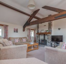 A living room with sofas coffee table stone fireplace and wooden ceiling beams at Lords Leap in Graythwaite near Hawkshead