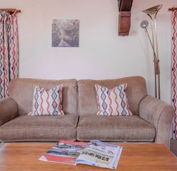 A living room with a brown sofa and patterned cushions next to windows with matching curtains and a coffee table with magazines at Lords Leap Graythwaite near Hawkshead