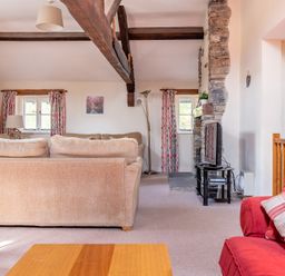 A living room with beige and red sofas exposed wooden beams and a stone fireplace at Lords Leap Graythwaite near Hawkshead