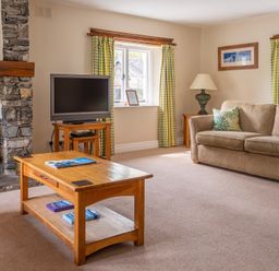 A living room with a beige sofa a wooden coffee table a flat screen tv on a stand and stone fireplace at Bassicks in Hawkshead