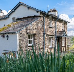 A stone and white plaster house with windows and a small porch surrounded by plants at Hilltop in Graythwaite near Hawkshead