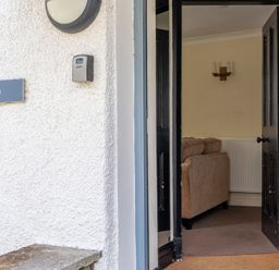 An open black door showing part of a beige sofa and radiator inside Hilltop in Graythwaite near Hawkshead