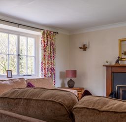 A living room with brown sofas a window with patterned curtains and a fireplace at Hilltop in Graythwaite near Hawkshead