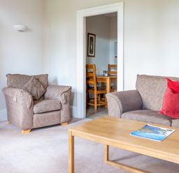 A living room with a brown armchair and sofa with red cushions and a wooden coffee table with a magazine at Mill Cottage in Graythwaite near Hawkshead