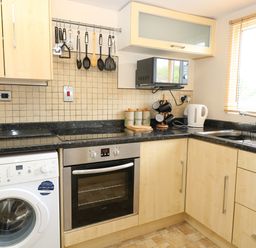 A kitchen with light wood cabinets a washing machine oven stovetop microwave kettle and sink at 2 Lock Cottages in Honing near East Ruston