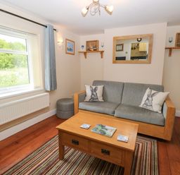 A living room with a grey sofa, wooden coffee table, striped rug, window with curtains, and wall shelves at 2 Lock Cottages in Honing near East Ruston