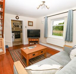 A living room with wooden floor a sofa a coffee table a television and a staircase at 2 Lock Cottages Honing near East Ruston