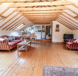 An attic living room with wooden floors wooden beams striped sofas a coffee table dining table and a kitchenette at Mrs Delaney's Loft in Ardfinnan near Clonmel County Tipperary