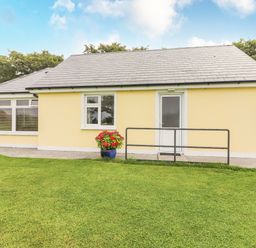 A yellow bungalow with a white door and windows on a lawn at Moybella Lodge in Lisselton near Ballybunion County Kerry