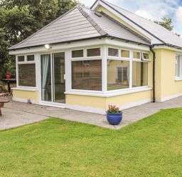 A yellow house with large windows and a concrete path with grass and potted plants at Moybella Lodge in Lisselton near Ballybunion County Kerry