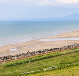 A beach with a railway track and grassy area at Morolwg in Llanaber near Barmouth