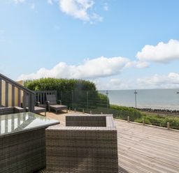 A wooden deck with outdoor wicker furniture and glass railing overlooking the sea at Morolwg in Llanaber near Barmouth