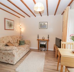 A living room with a floral sofa a small fireplace a television a wooden dining table with flowers and a window with curtains at Woods Edge in Mitcheldean