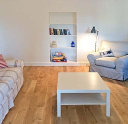 A living room with a couch, armchair, white coffee table, built-in bookshelf, and floor lamp at The Grange in Little Haven near Haverfordwest