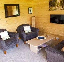 A sitting area with two armchairs a sofa a coffee table and a wall-mounted television at Pennylands Willow Lodge in Broadway